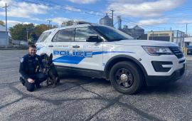 Police officer kneeling next to canine officer with Police car in the background